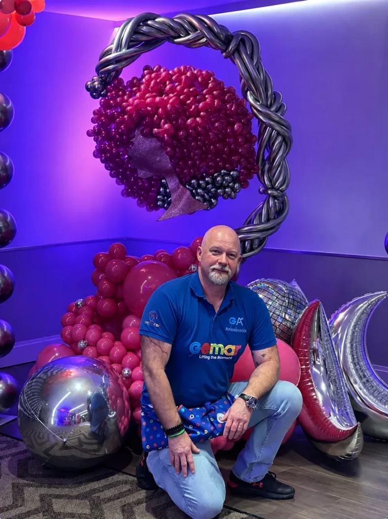 Tampilipe in a Gemar polo shirt kneeling in front of a balloon installation