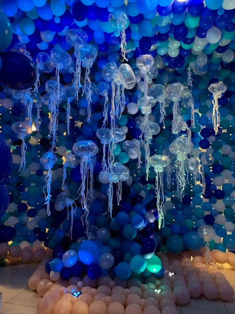 Salle sur le th&egrave;me des fonds marins avec un mur de ballons bleus et des m&eacute;duses en ballons suspendues