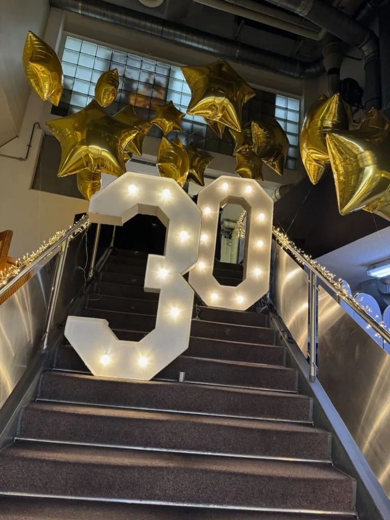 Chiffre lumineux 30 sur un escalier avec des ballons étoiles dorés