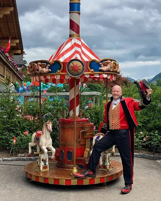Tampilipe in a red ringmaster coat next to a vintage carousel