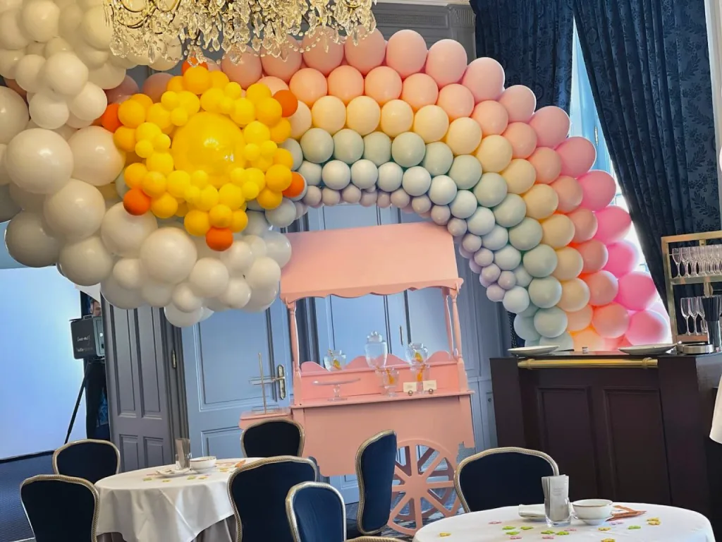 Arche de ballons arc-en-ciel avec nuages et soleil au-dessus d&rsquo;un chariot &agrave; bonbons